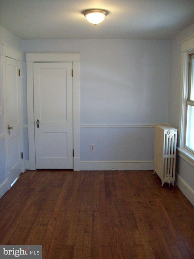 unfurnished room with baseboards, hardwood / wood-style floors, and radiator heating unit