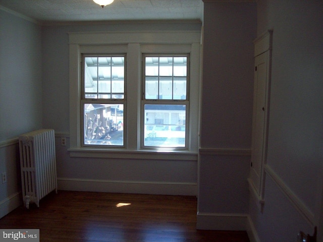 empty room featuring ornamental molding, radiator heating unit, baseboards, and wood finished floors