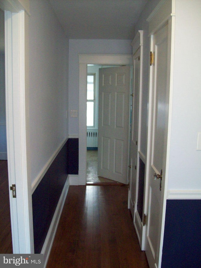 hallway with radiator, wood finished floors, and baseboards