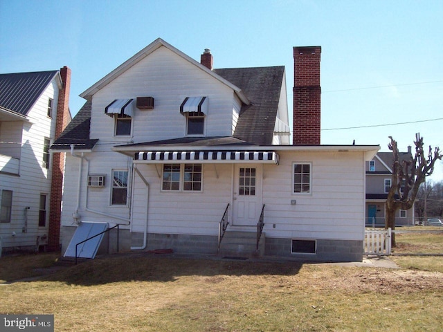 rear view of property with a shingled roof, a lawn, entry steps, and a chimney