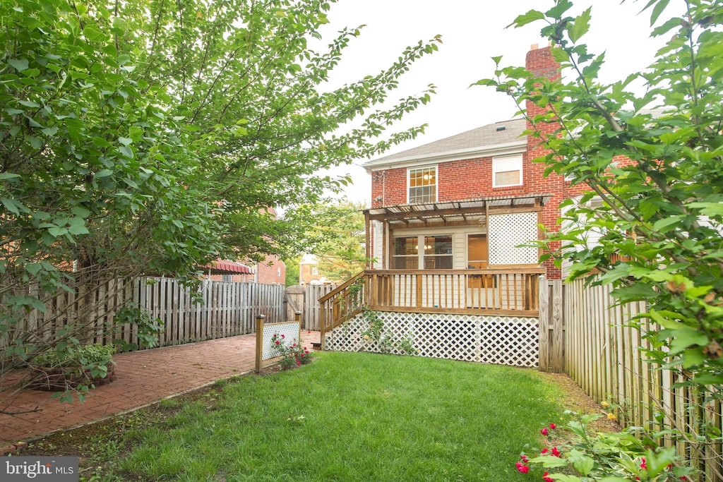 rear view of house with a wooden deck, a fenced backyard, a chimney, a lawn, and brick siding