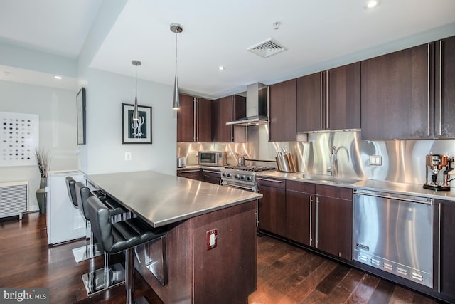 kitchen featuring visible vents, a sink, stainless steel counters, appliances with stainless steel finishes, and wall chimney range hood