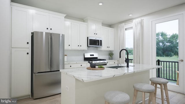 kitchen with an island with sink, stainless steel appliances, light wood-style floors, white cabinetry, and a sink