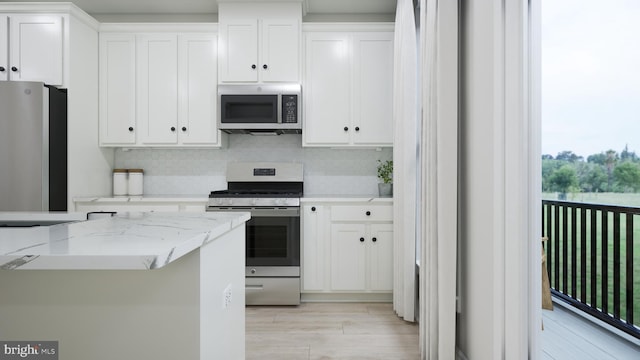 kitchen with light stone countertops, light wood-style flooring, white cabinets, appliances with stainless steel finishes, and tasteful backsplash