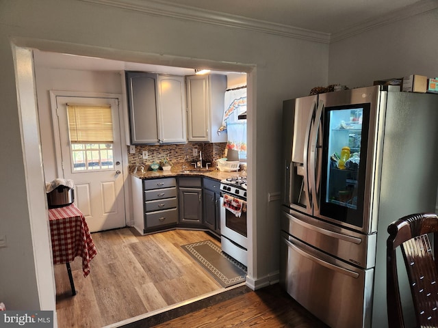 kitchen with light wood finished floors, gray cabinetry, ornamental molding, decorative backsplash, and appliances with stainless steel finishes