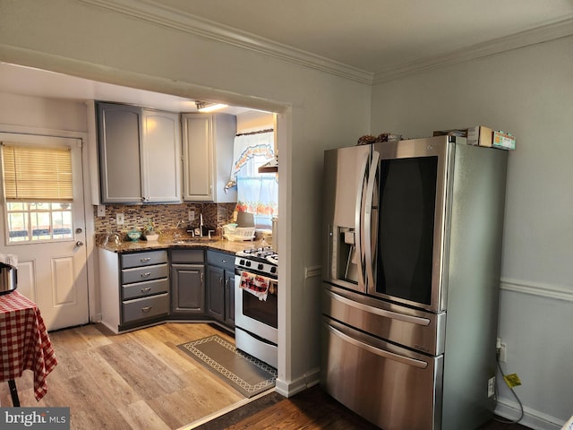 kitchen featuring gray cabinetry, light wood-style flooring, backsplash, stainless steel appliances, and crown molding