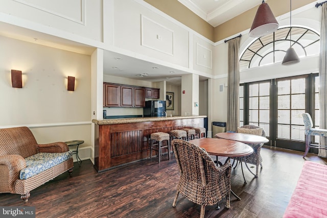 dining space featuring dark wood-style floors, crown molding, a high ceiling, and baseboards