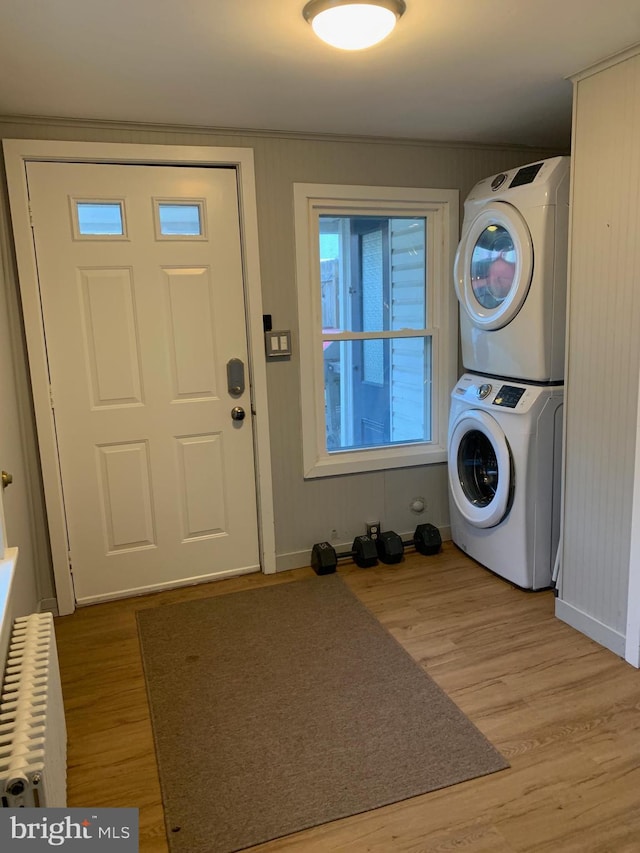 clothes washing area with laundry area, radiator, stacked washer / drying machine, and wood finished floors