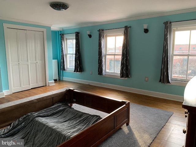 bedroom with ornamental molding, wood finished floors, radiator heating unit, a closet, and baseboards