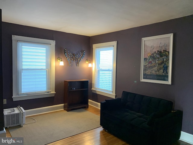 sitting room with a wall mounted air conditioner, baseboards, and wood finished floors