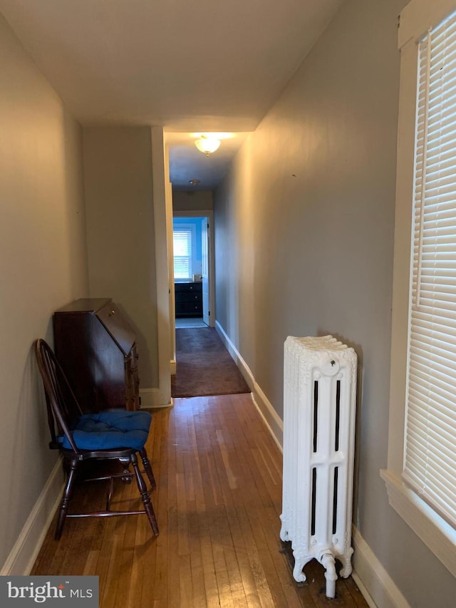 hall featuring baseboards, radiator, and hardwood / wood-style floors