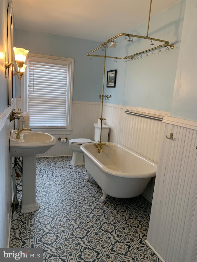 full bathroom featuring tile patterned floors, a freestanding tub, a wainscoted wall, toilet, and a sink