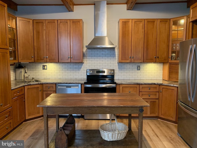 kitchen featuring light wood finished floors, stainless steel appliances, wall chimney range hood, and a sink