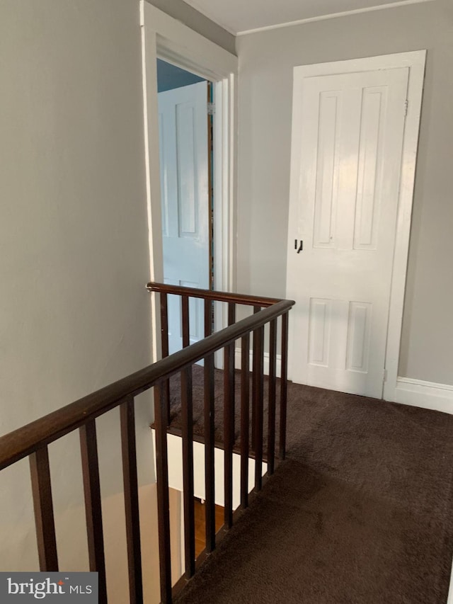 corridor with an upstairs landing and dark colored carpet