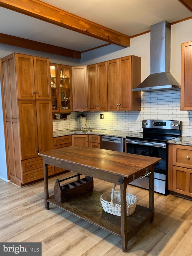 kitchen with light wood finished floors, decorative backsplash, stainless steel appliances, and wall chimney exhaust hood