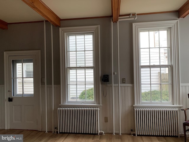 doorway with beamed ceiling, radiator heating unit, wood finished floors, and wainscoting