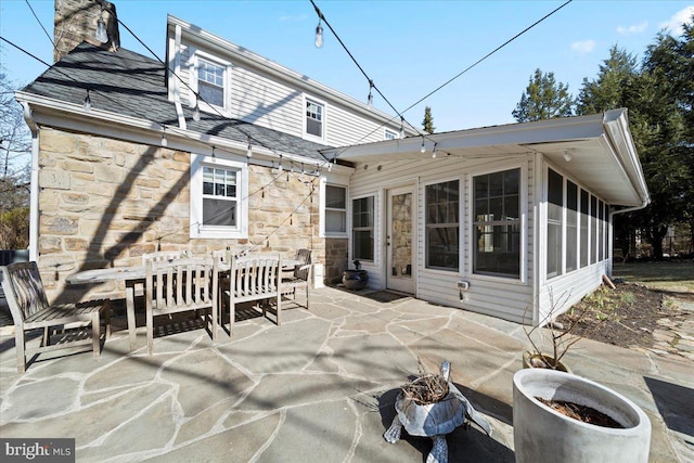 rear view of property featuring stone siding, a chimney, outdoor dining area, and a patio