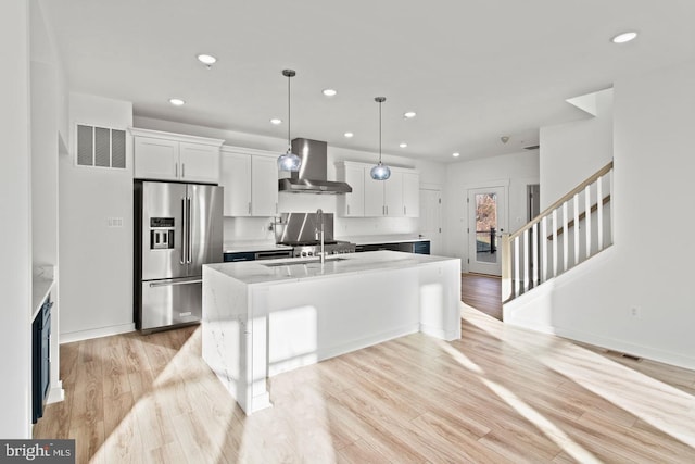 kitchen with visible vents, an island with sink, light wood-style flooring, stainless steel refrigerator with ice dispenser, and wall chimney exhaust hood