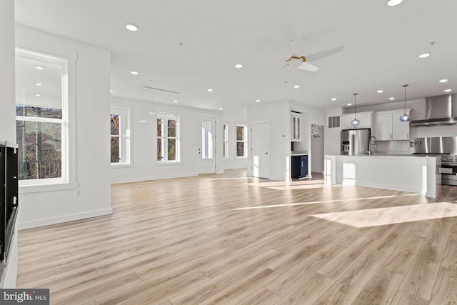 unfurnished living room featuring a ceiling fan, baseboards, recessed lighting, a sink, and light wood-style floors