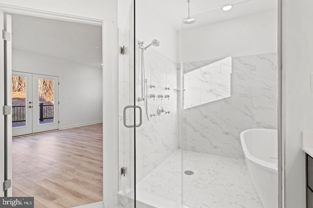 bathroom featuring wood finished floors, baseboards, a marble finish shower, a soaking tub, and french doors