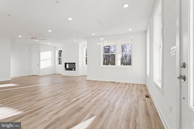 unfurnished living room featuring light wood-style flooring, a glass covered fireplace, recessed lighting, baseboards, and ceiling fan