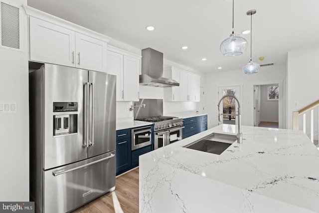 kitchen with high quality appliances, a sink, blue cabinetry, white cabinetry, and wall chimney exhaust hood