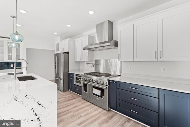 kitchen with light wood finished floors, premium appliances, white cabinetry, wall chimney exhaust hood, and a sink