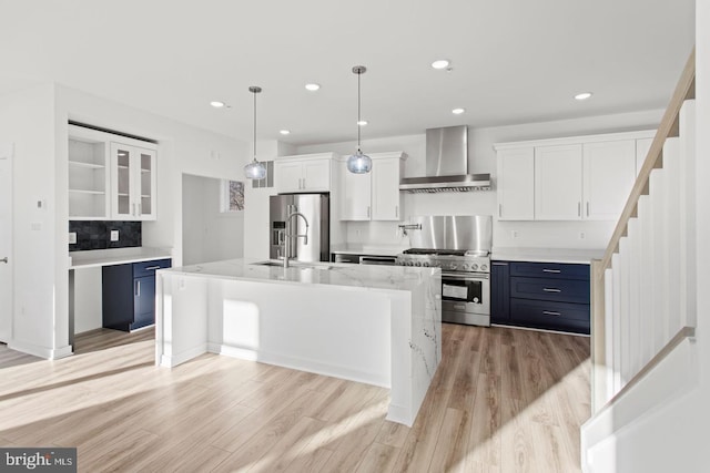 kitchen with wall chimney range hood, white cabinets, appliances with stainless steel finishes, and a sink