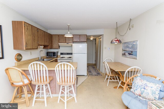 kitchen with under cabinet range hood, light countertops, a peninsula, white appliances, and a sink