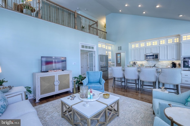 living room with recessed lighting, wood finished floors, visible vents, and high vaulted ceiling