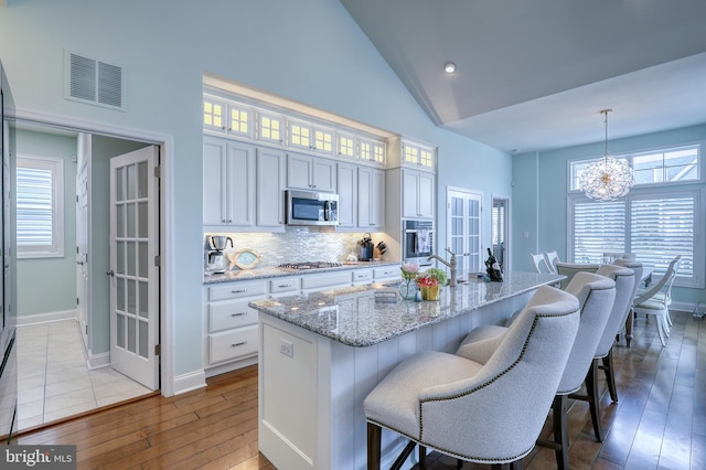 kitchen featuring visible vents, a chandelier, appliances with stainless steel finishes, white cabinets, and high vaulted ceiling