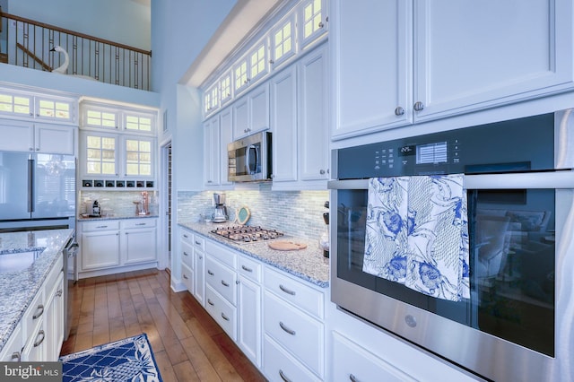 kitchen featuring tasteful backsplash, glass insert cabinets, stainless steel appliances, white cabinetry, and dark wood-style flooring