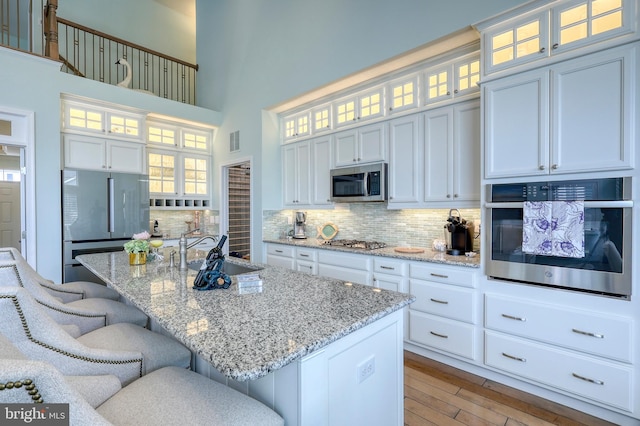 kitchen featuring a kitchen bar, decorative backsplash, white cabinets, stainless steel appliances, and a sink