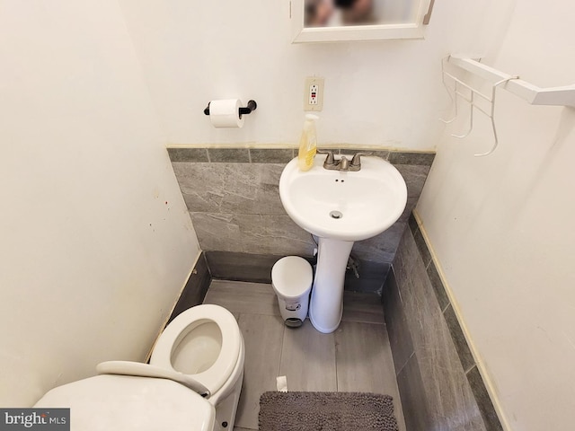 half bath with tile walls, toilet, and a sink