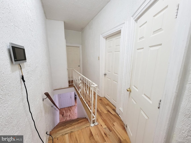 stairway featuring a textured ceiling, wood finished floors, and a textured wall