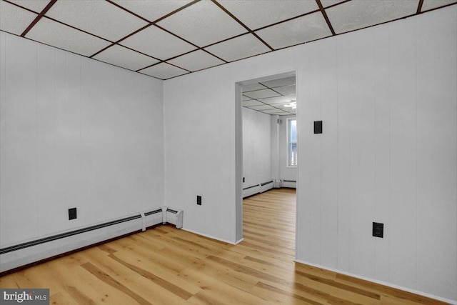 below grade area featuring a paneled ceiling, baseboard heating, and wood finished floors