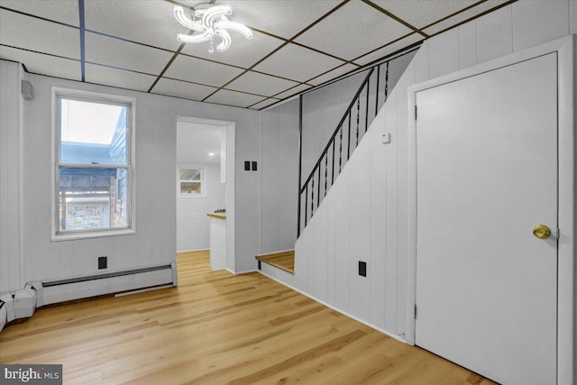 interior space with stairs, wood finished floors, a baseboard heating unit, and a paneled ceiling