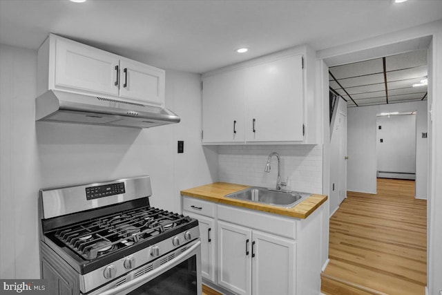 kitchen featuring gas stove, a sink, under cabinet range hood, white cabinetry, and butcher block counters