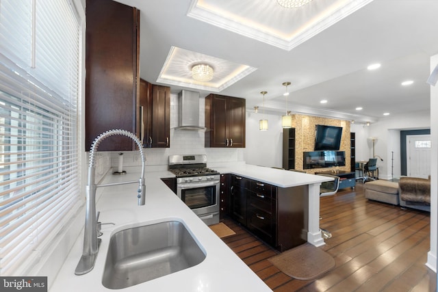 kitchen with stainless steel gas range oven, wall chimney range hood, open floor plan, a peninsula, and a sink