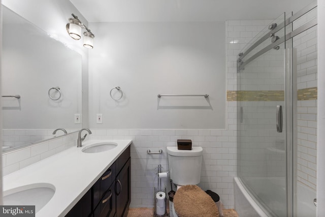 full bath featuring toilet, a sink, tile walls, wainscoting, and double vanity