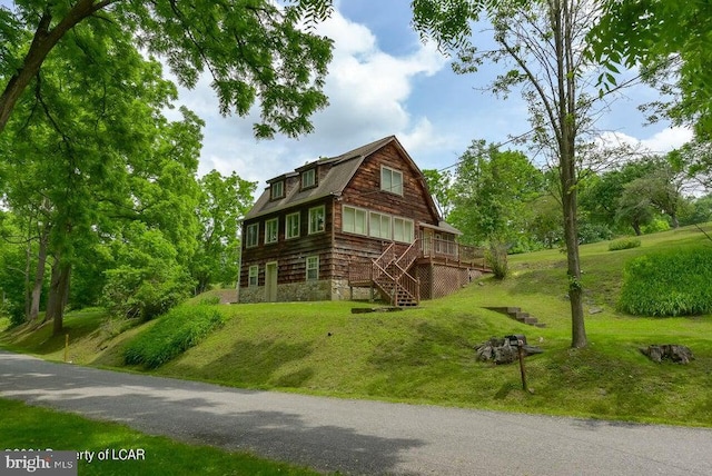 view of side of property with a wooden deck, a gambrel roof, a lawn, and stairs