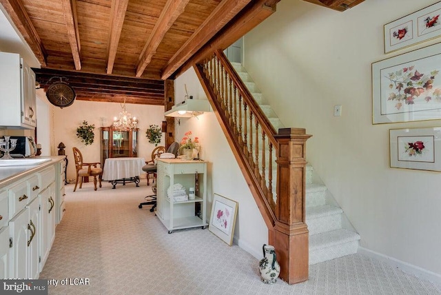 stairway with baseboards, a chandelier, beam ceiling, carpet flooring, and wooden ceiling