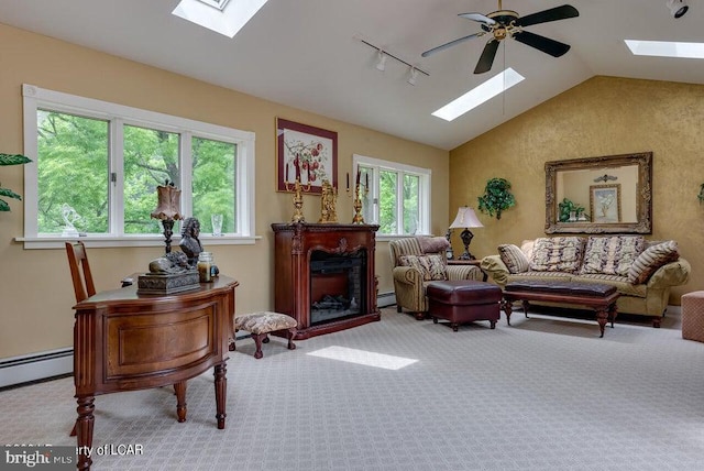 living area with track lighting, a ceiling fan, a baseboard heating unit, vaulted ceiling with skylight, and carpet