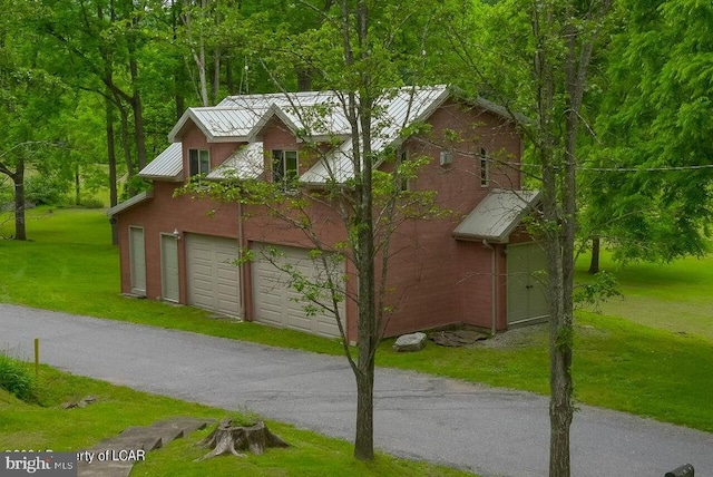 view of side of home with a forest view, aphalt driveway, a lawn, metal roof, and a garage