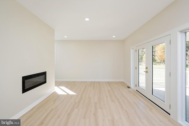 unfurnished living room with wood finished floors, french doors, baseboards, and a glass covered fireplace