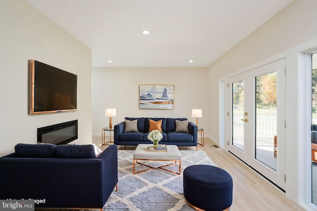 living room with light wood-style flooring, a glass covered fireplace, recessed lighting, french doors, and baseboards