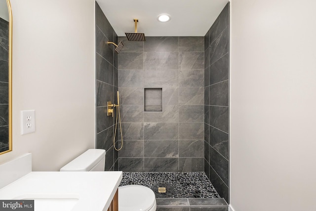 full bathroom featuring tiled shower, toilet, and vanity