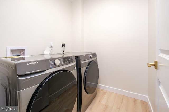 washroom featuring laundry area, washing machine and dryer, light wood-style floors, and baseboards