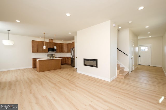 kitchen with light wood finished floors, open floor plan, appliances with stainless steel finishes, and an island with sink