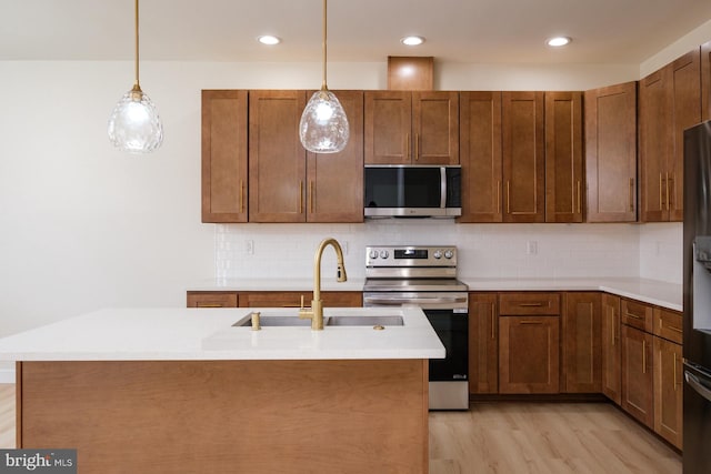 kitchen with light wood finished floors, light countertops, decorative backsplash, appliances with stainless steel finishes, and a sink